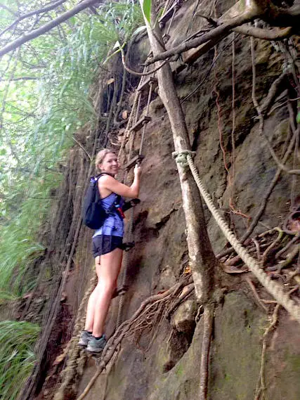 Woman climbing down a root covered cliff using a rope ladder.