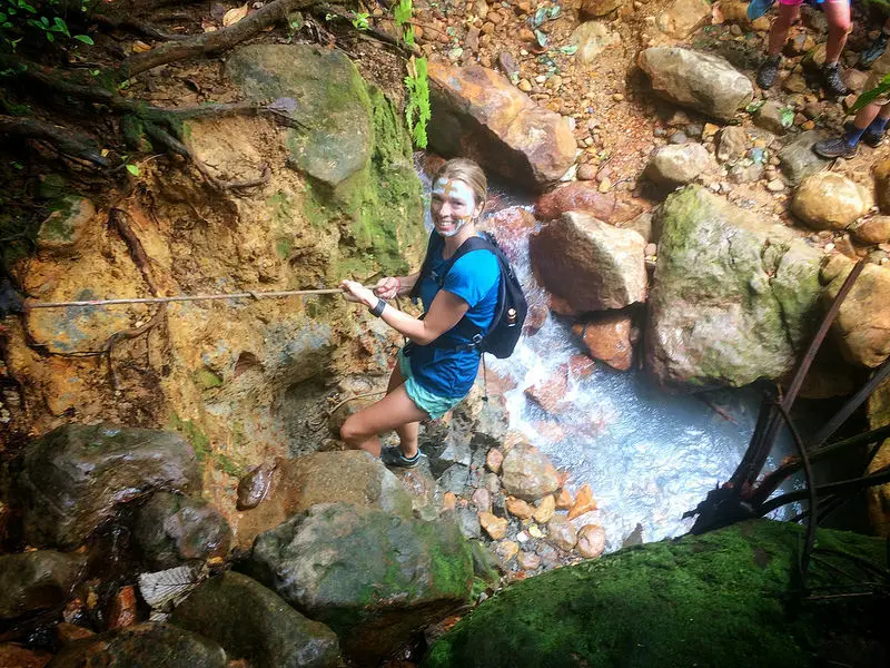 Woman using a rope to climb down a cliff to a sulphur hot spring river on the way to Boiling Lake, Dominica.