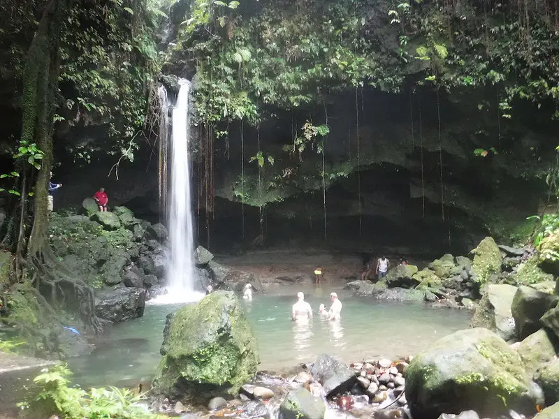 People bathing at the base of a waterfall on a cliff edge in Dominica.
