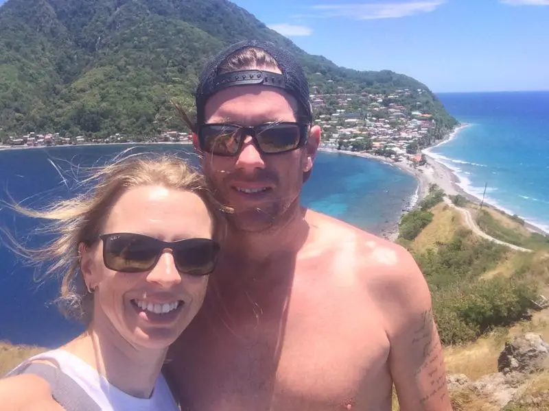 Couple selfie with green hills and turquoise waters of Dominica behind.