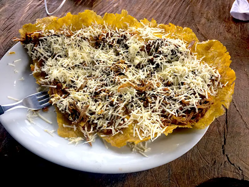 Plate covered in a patacon with meat and cheese.