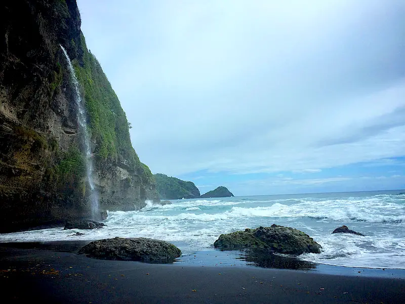 Black sand beach with a waterfall coming over the cliff and falling into the Caribbean Sea at Wavine Cyrique, Dominica.
