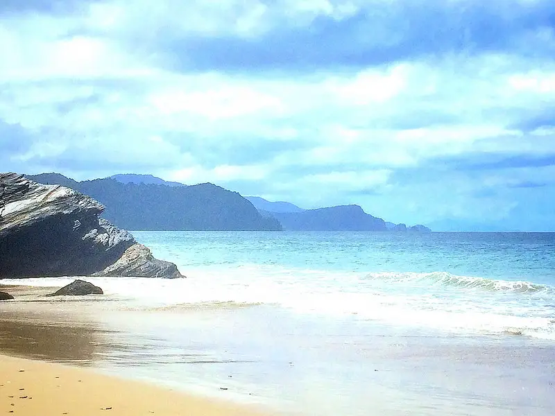 Beautiful Caribbean beach with golden sand and mountain backdrop with stormy sky in Trinidad.