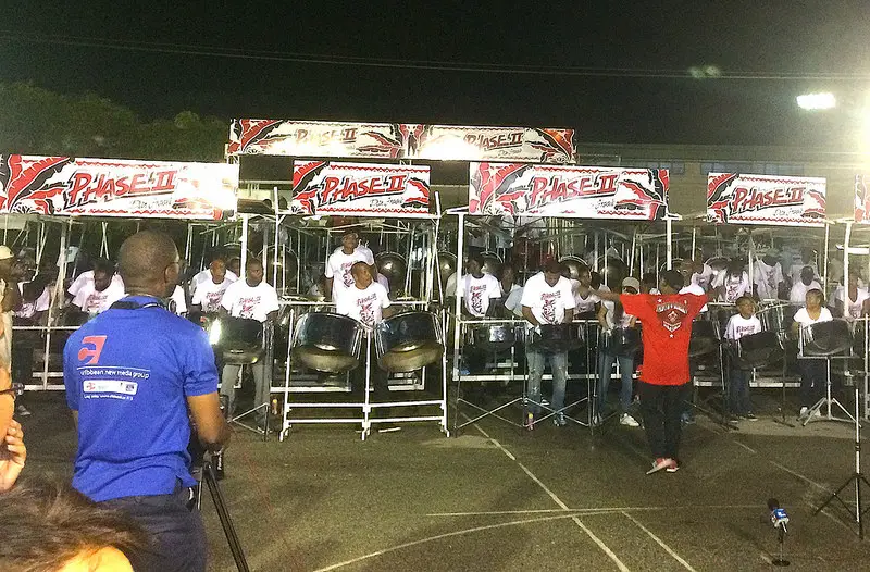 group of people playing steel pan drums at night with a conductor leading them