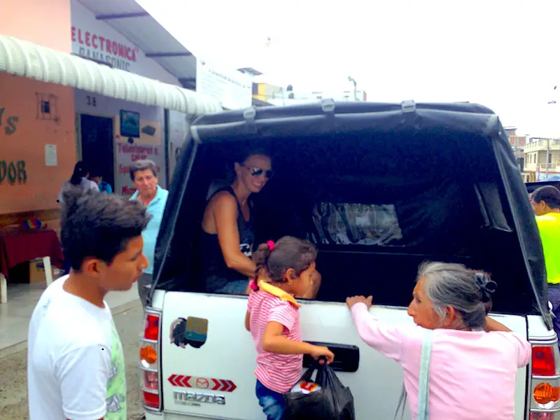 Elder lady and young girl climbing in the back of a pickup truck taxi to Santa Marianita, Ecuador