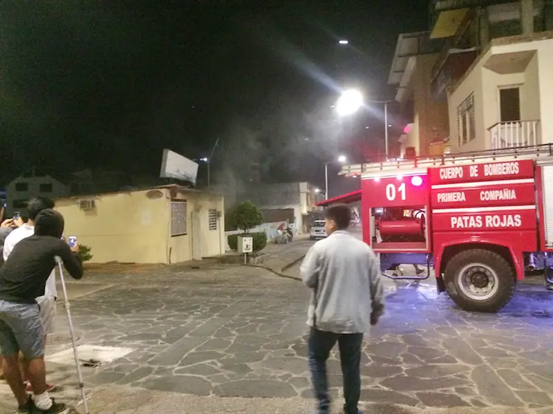 Smoke billowing out a doorway with a firetruck parked in the road and people standing around watching in San Cristobal Island, Galapagos