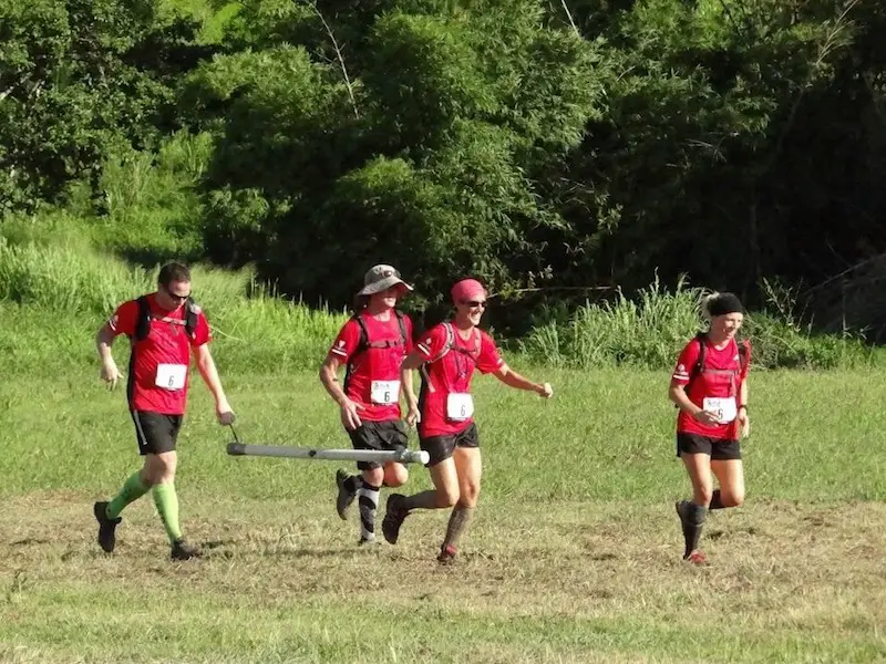 Four people in matching red shirts and team numbers running through a field to finish an adventure race in Trinidad.