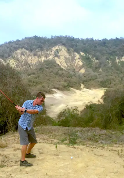 Man swinging a golf club across a ravine on a future golf course in Ecuador.