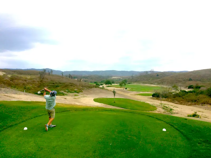 Man swinging a golf club on a green tee block at Montecristi Golf Club in Ecuador.