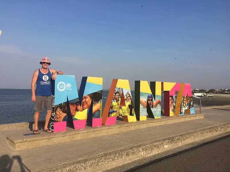 Man standing beside a brightly coloured large Manta sign on the coast, Ecuador.