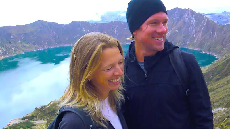 Laughing couple with emerald coloured Quilotoa Lake and mountains behind in Ecuador.