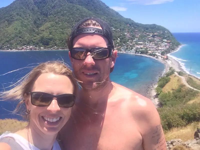 Couple selfie on top of Scotts Head Peninsula in Dominica with bright blue Caribbean Sea behind.