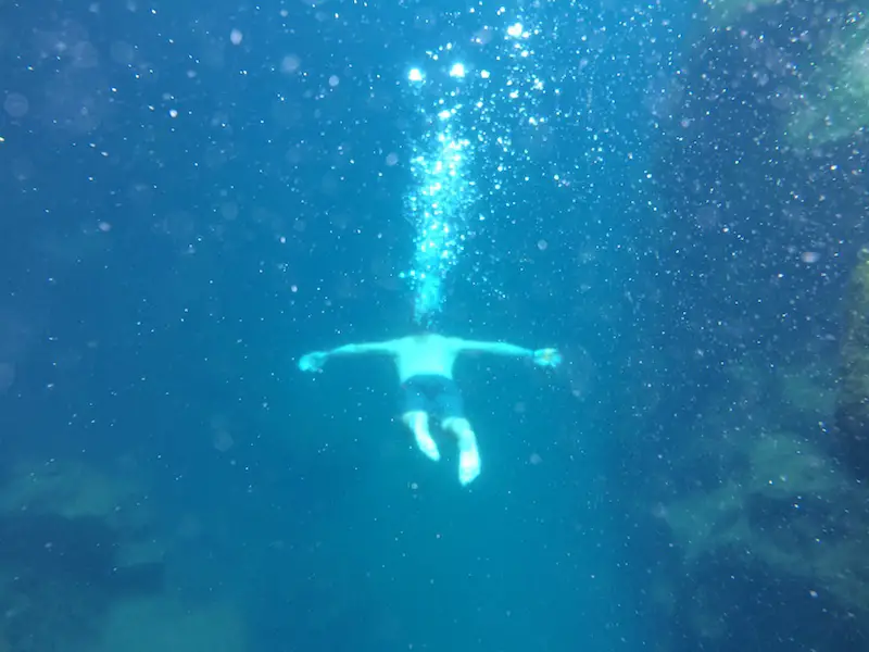 Man swimming through water with bubbles leading from him up to the surface at Las Grietas, Galapagos Islands.