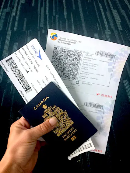 Hand holding Canadian passport, plane ticket and visa to visit Galapagos Islands, Ecuador.