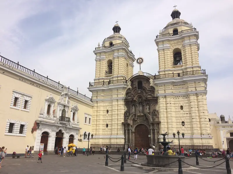 Yellow ornate building of a church and convent in Lima Peru with plaza in front.