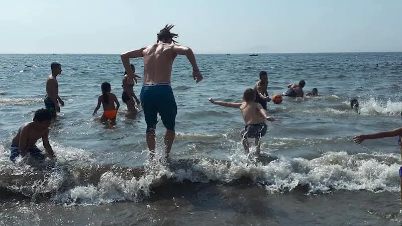 Man and boy jumping over waves at a busy beach in Lima, Peru.