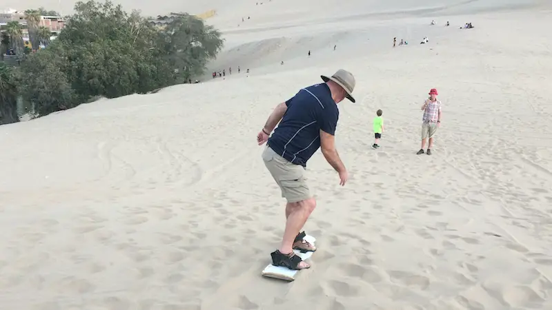 Man sand boarding down a huge sand dune in Huacachina, Peru