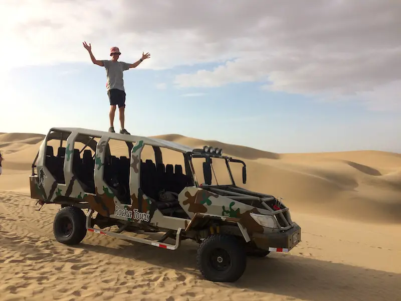 Man standing on top of a dune buggy in camouflage paint in the desert.