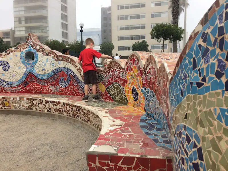 A boy rolling his soccer ball along the undulating edge of a mosaic bench at Parque del Amor in Lima, Peru.