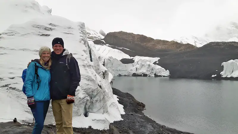 Man and woman standing in front of a glacier creeping into a lake in Pastoruri Peru.