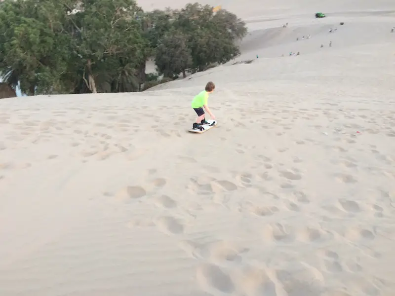 Young boy sand boarding down a huge sand dune in Huacachina, Peru.