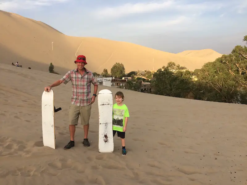 Man and boy standing in sand dunes holding sandboards in Huacachina, Peru.