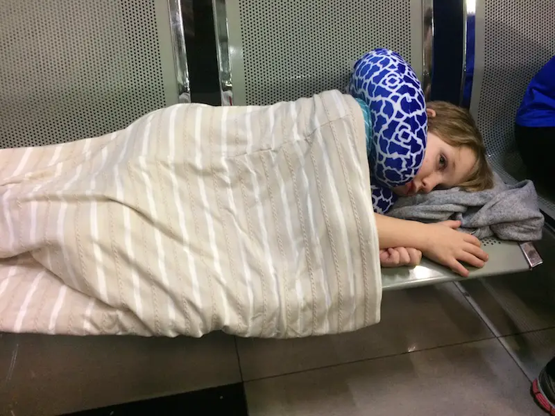 Boy laying on a bench with a scarf and head pillow to sleep.