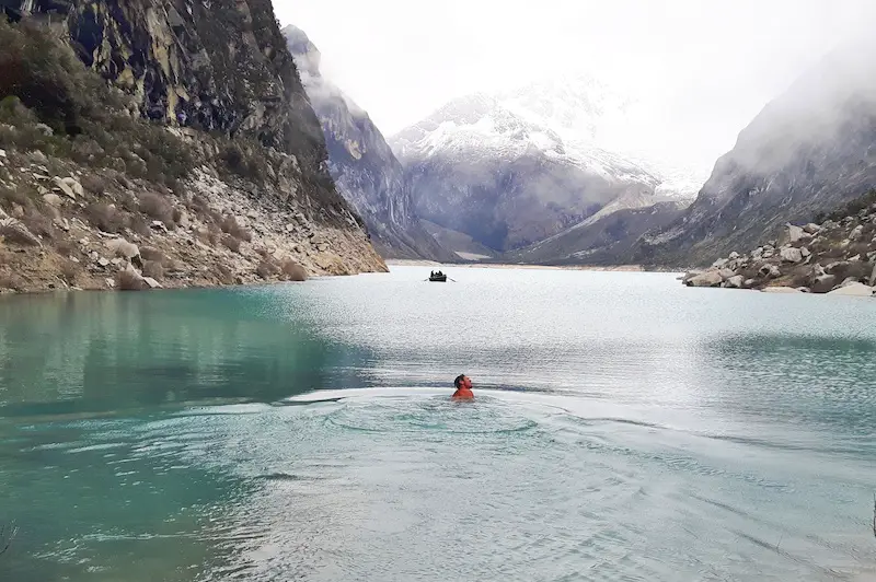 Man swimming in a glacier lake surrounded by mountains in Paramount Lake, Peru.
