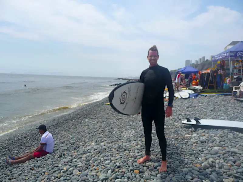 Man in wetsuit holding surfboard ready to go into the water at Miraflores beach in Lima, Peru.