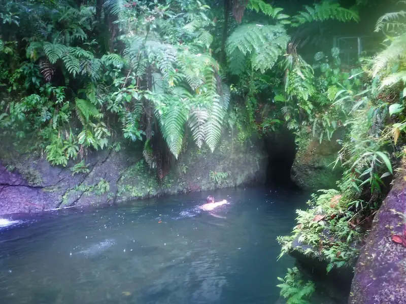 Man swimming into the opening of Titou Gorge, Dominica surrounded by lush jungle.