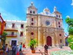 Stone cathedral with a sculpture plaza in front and a bright blue sky, Cartagena, Colombia.