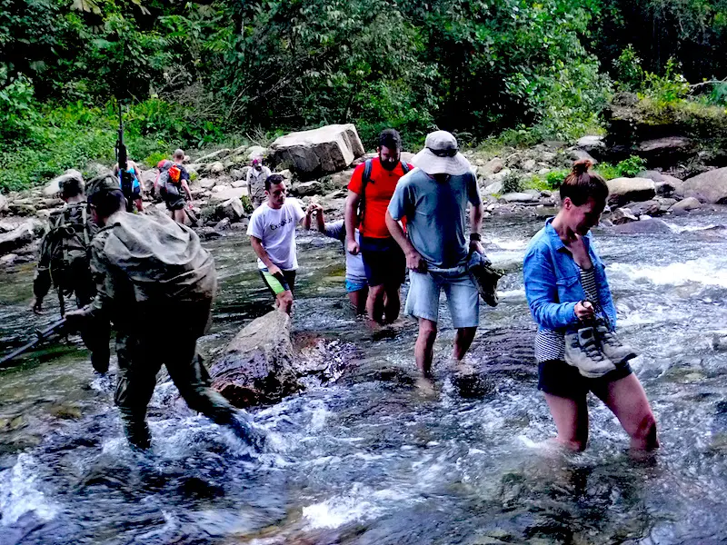 Hikers passing soldiers while crossing a river on the trail to the Lost City, Colombia.