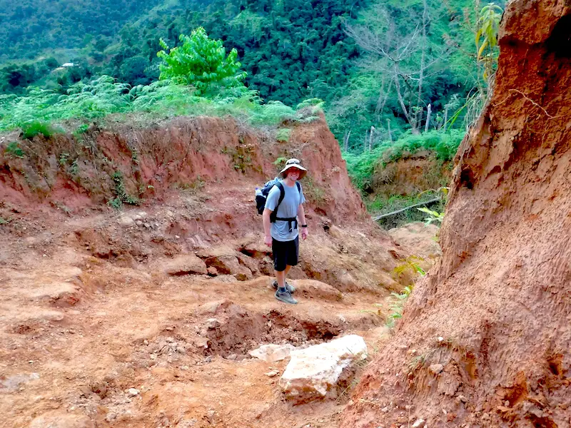 Man hiking through deep red clay gorge in mountainside on Lost City Trek, Colombia.