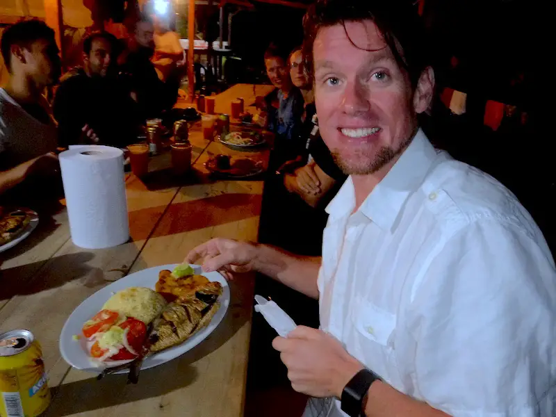 Man smiling with his dinner of fried fish, rice and salad in a camp for Lost City trek, Colombia