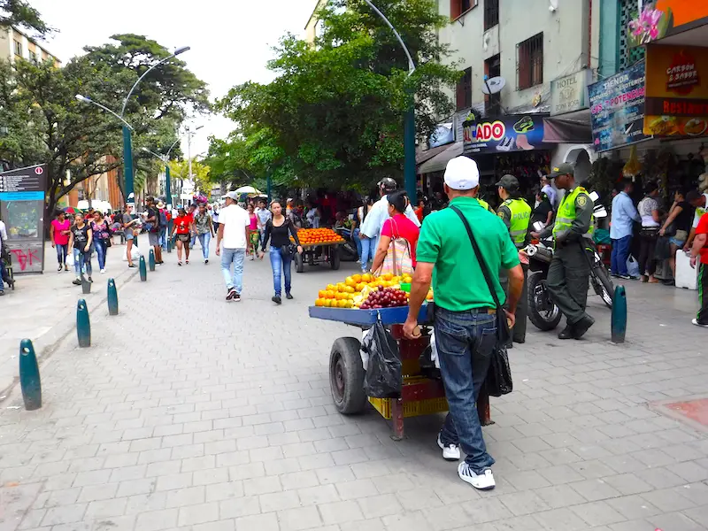 Man walking with a cart full of fruit down a busy pedestrian street in Medellin, Colombia.