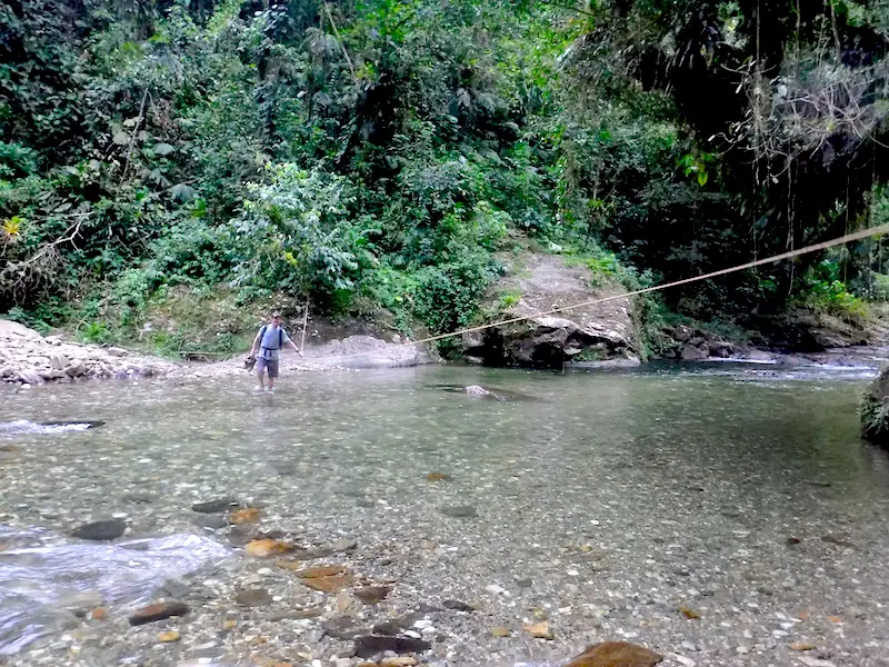 Man wading through wide rocky river on Lost City trek, colombia.