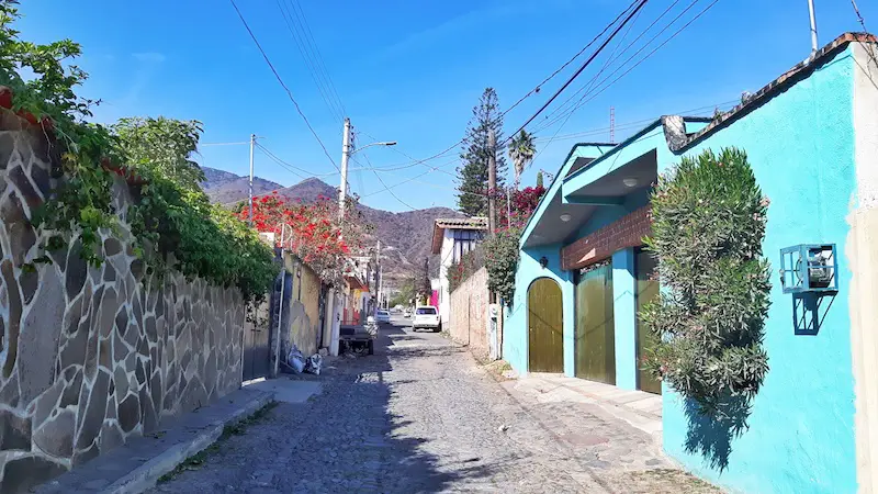 Cobblestone street with colour houses and flowers on each side and mountains in the distance in Mexico.