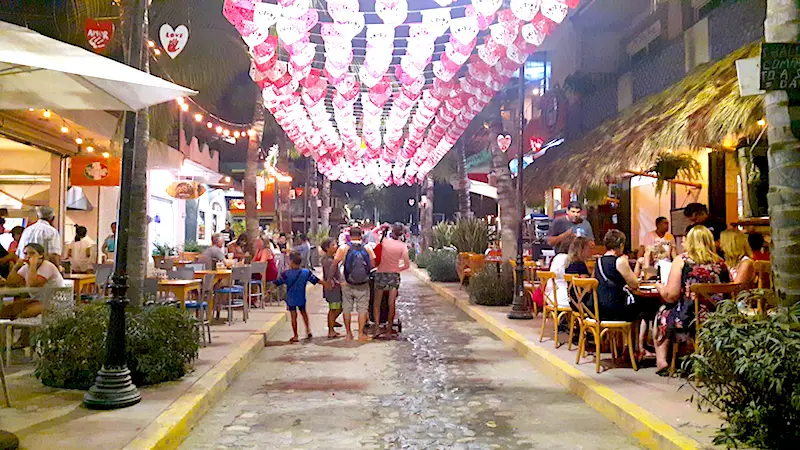 Cobble street lined with restaurants and pink and white banners overhead in Sayulita, Mexico.