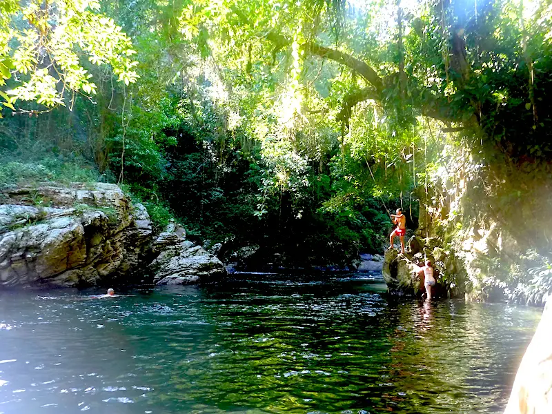Man swinging from rope swing into river surrounded by jungle in Colombia.
