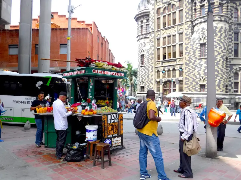 Man at a fruit stand in downtown Medellin with other people moving around.