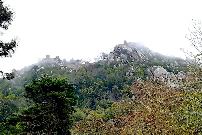 Looking up at a moorish castle on a hill between clouds in Sintra, Portugal