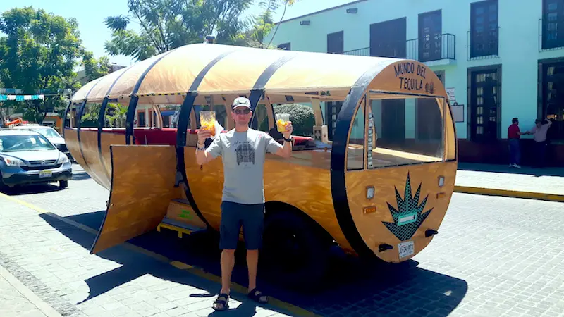 Man holding snacks outside a vehicle shaped like a barrel for a tequila tour in Tequila, Mexico.