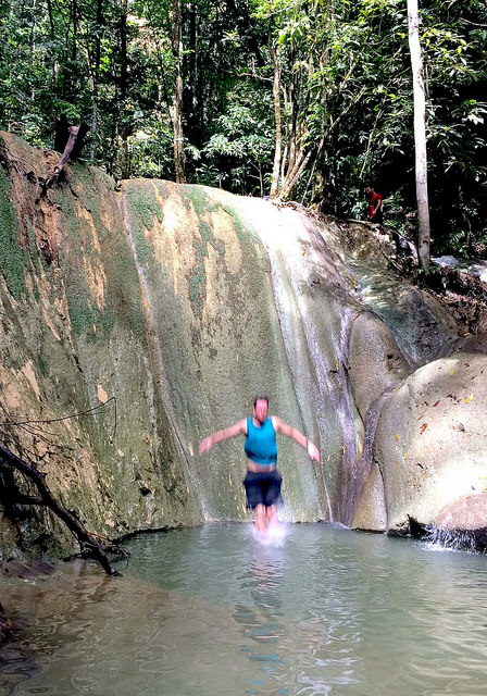 Man jumping over a waterfall with a large limestone wall behind.