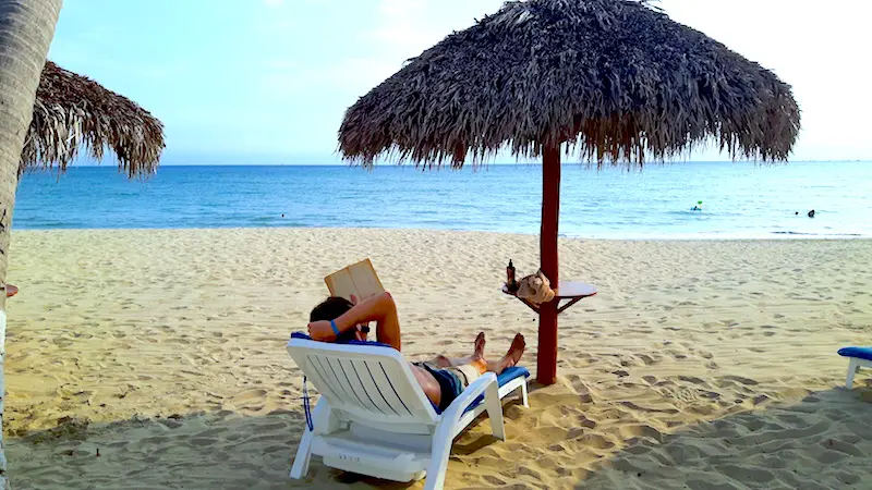 Man on a sun lounger under a palapa reading a book on the beach in Bucerias, Mexico.