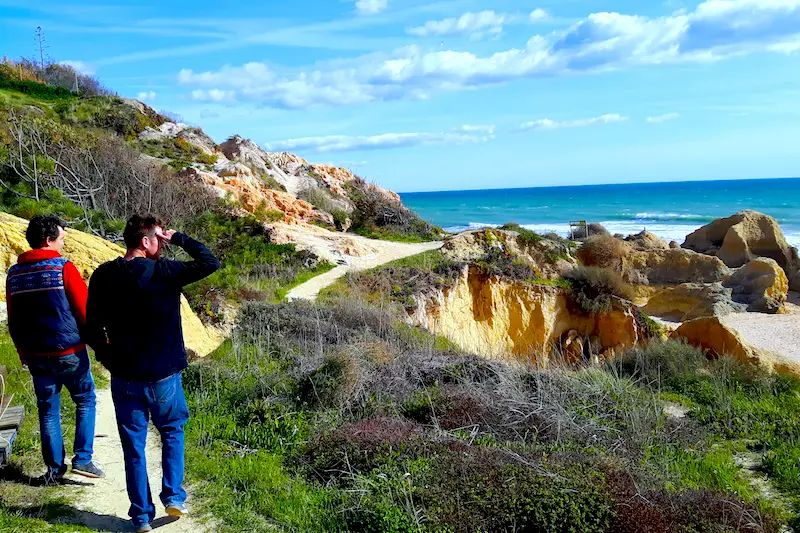 Two men walking along a cliff looking out to sea in the Algarve, Portugal.