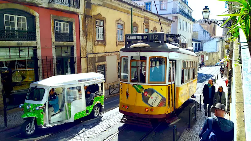 Yellow tram and green tuk-tuk on an old street in Lisbon Portugal.