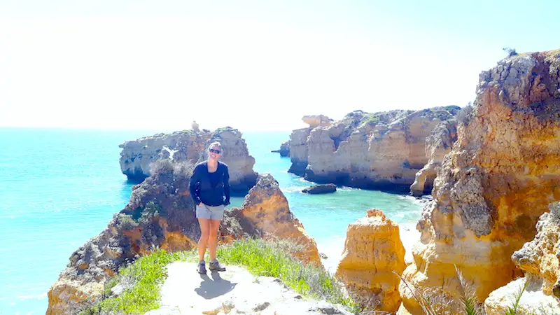 Woman standing on a cliff with rock formations and blue Atlantic Ocean behind in Algarve, Portugal