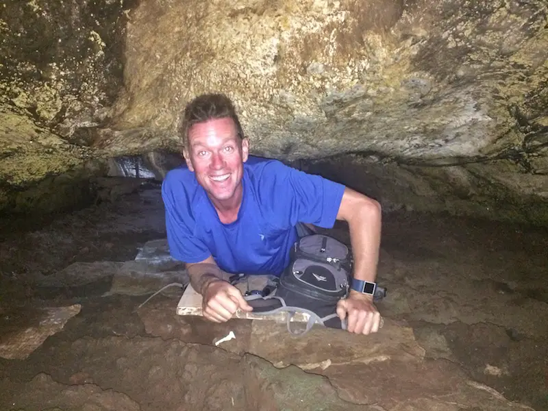 Man laying on stomach crawling through a crack in a lava tube, Galapagos.