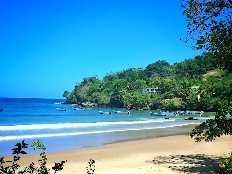 Fishing boats in the water at the end of a bay with golden sand and blue water at Las Cuevas in Trinidad