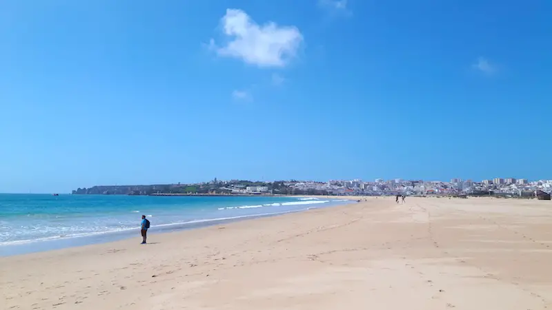 A huge beach with a glimpse of a town at the far end in Lagos, Portugal.